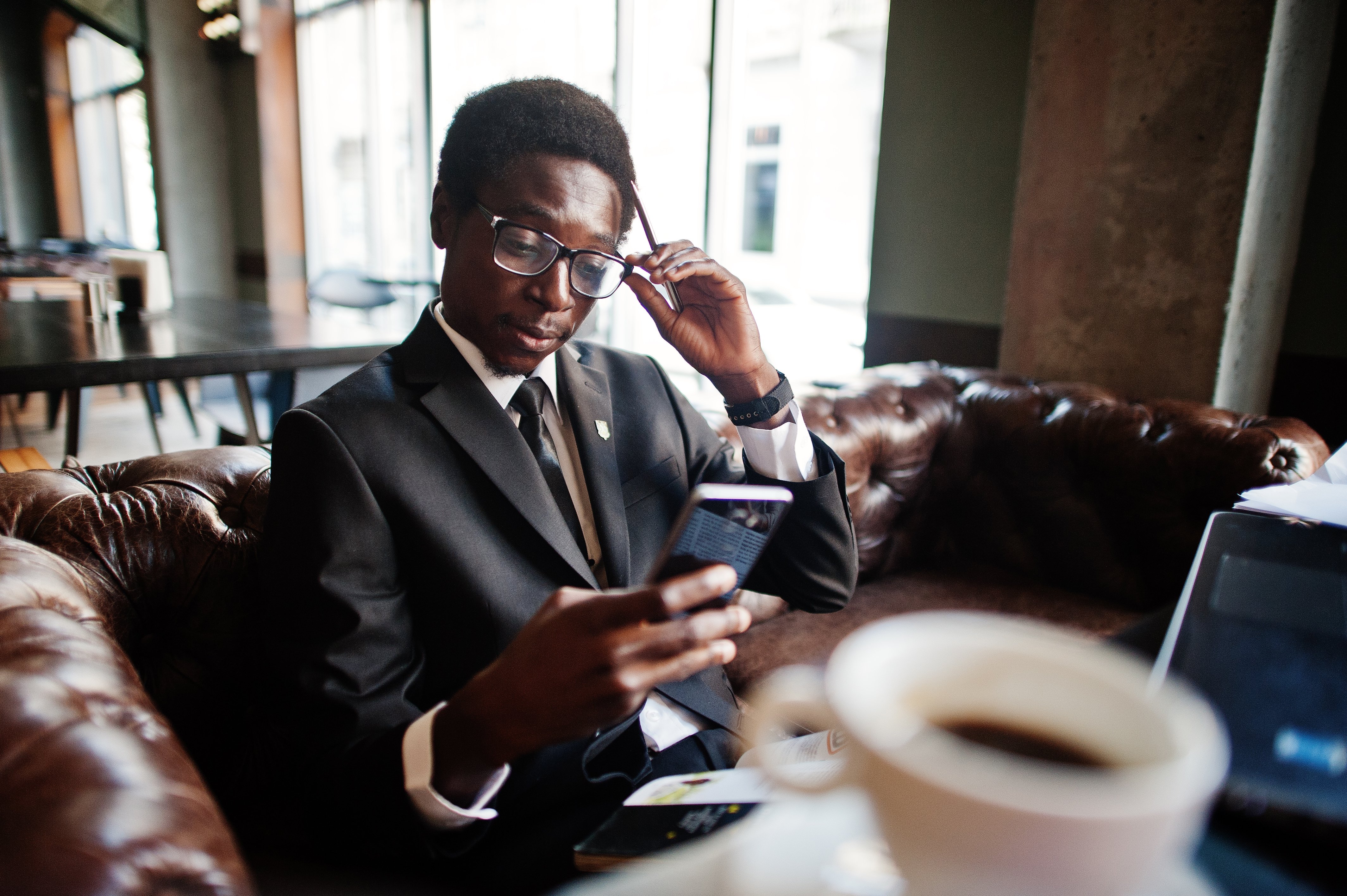 business-african-american-man-wear-black-suit-glasses-sitting-office-with-laptop-working-looking-mobile-phone